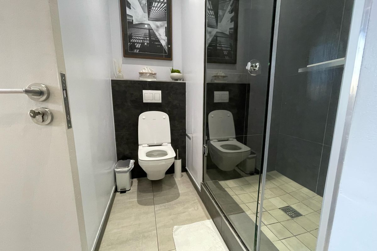 Modern bathroom featuring a wall-hung toilet with a concealed cistern and a glass-enclosed shower with dark tiled accents.