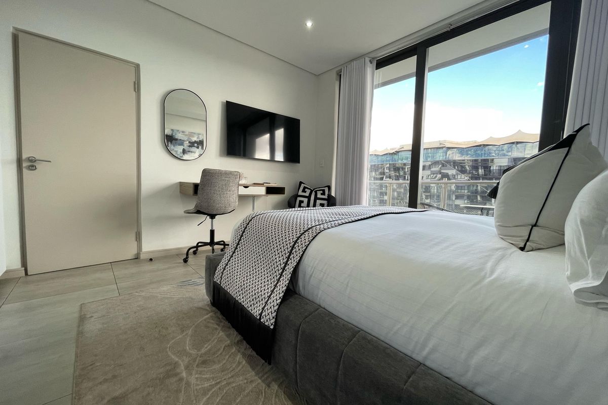 Modern bedroom featuring large sliding glass doors with natural light, neutral tiled flooring, and recessed ceiling lighting.