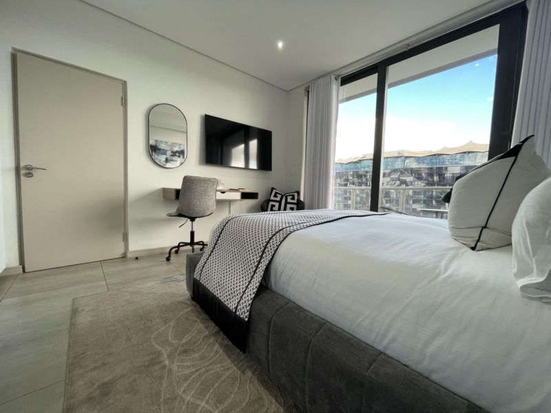 Modern bedroom featuring large sliding glass doors with natural light, neutral tiled flooring, and recessed ceiling lighting.