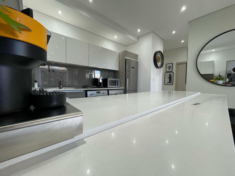 Modern kitchen featuring sleek gloss cabinetry, high-quality quartz countertops, integrated appliances, and recessed downlighting in a contemporary open-plan layout.