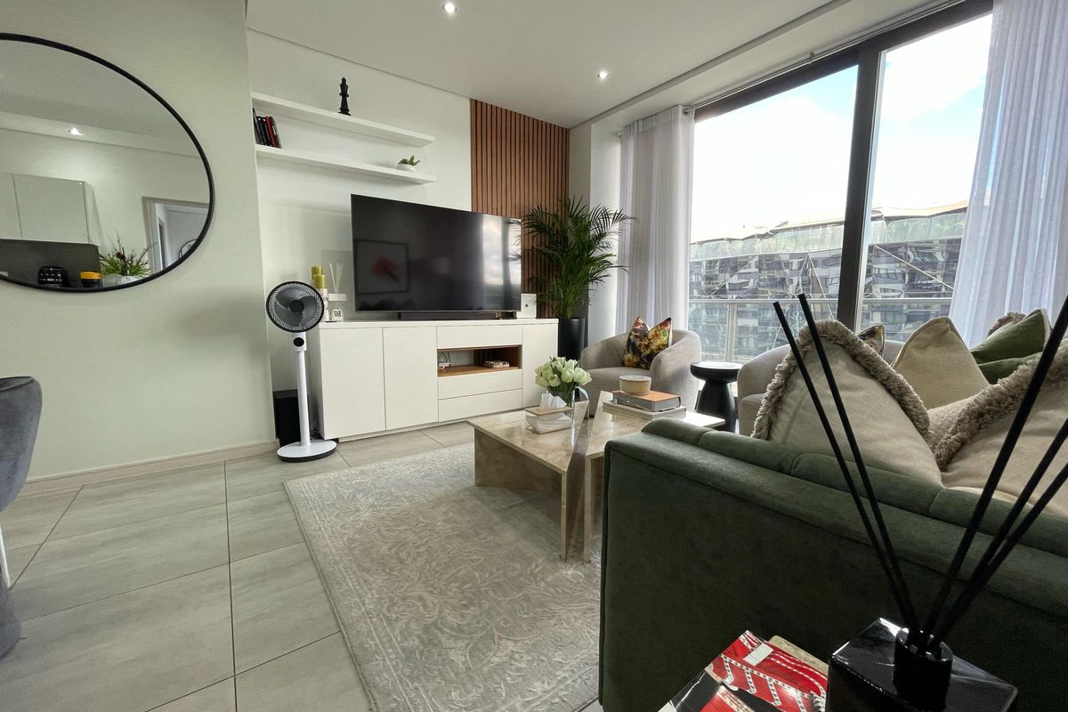 Modern living room featuring large floor-to-ceiling windows, sleek tiled flooring, and stylish built-in shelving with decorative wood wall paneling.