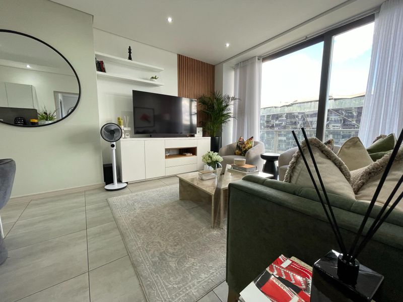 Modern living room featuring large floor-to-ceiling windows, sleek tiled flooring, and stylish built-in shelving with decorative wood wall paneling.