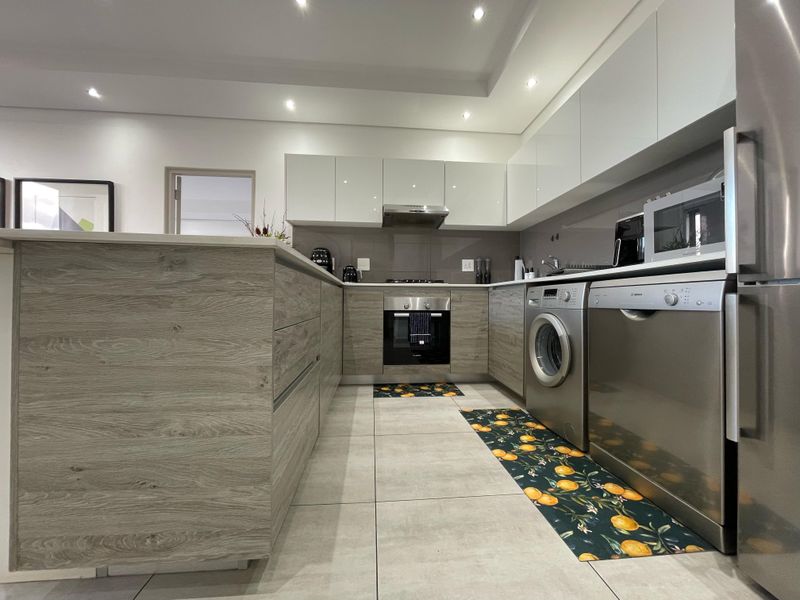 Modern kitchen featuring sleek wood-grain cabinetry, stone countertops, integrated appliances, and recessed lighting in a clean, contemporary layout.