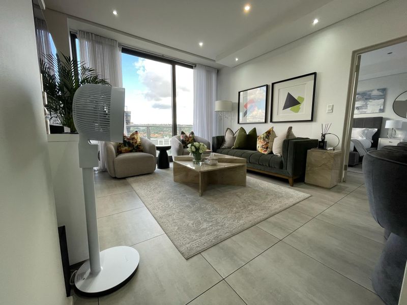 Modern living room featuring large floor-to-ceiling windows with natural light, recessed downlighting, and neutral tiled flooring, offering a bright and contemporary atmosphere.