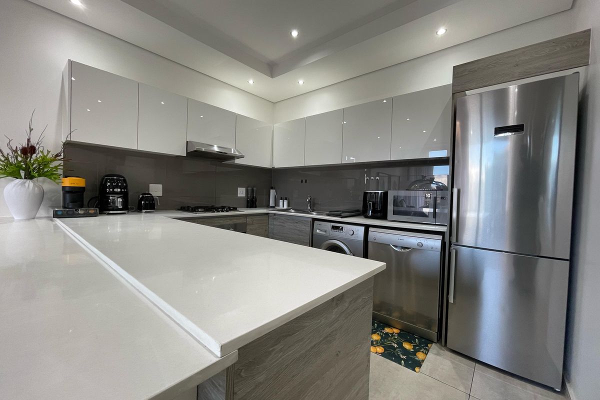 Modern kitchen featuring sleek glossy cabinetry, quartz countertops, integrated stainless steel appliances, and recessed lighting in a clean, contemporary layout.