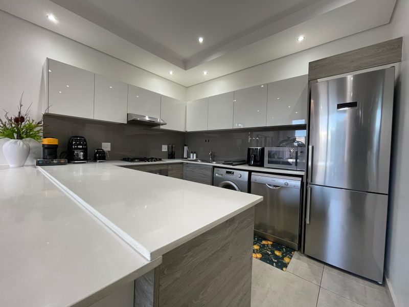 Modern kitchen featuring sleek glossy cabinetry, quartz countertops, integrated stainless steel appliances, and recessed lighting in a clean, contemporary layout.