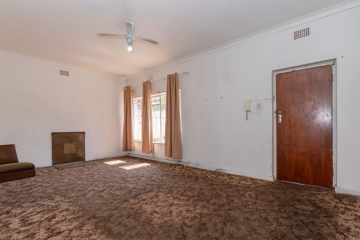 Spacious living room featuring a fireplace, ceiling fan, and security gate, offering a blank canvas for renovation and modernization.