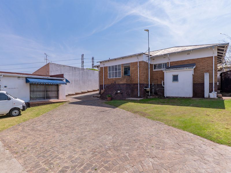 Rear view of the property featuring a paved driveway, lawn area, and brick exterior walls with security features.