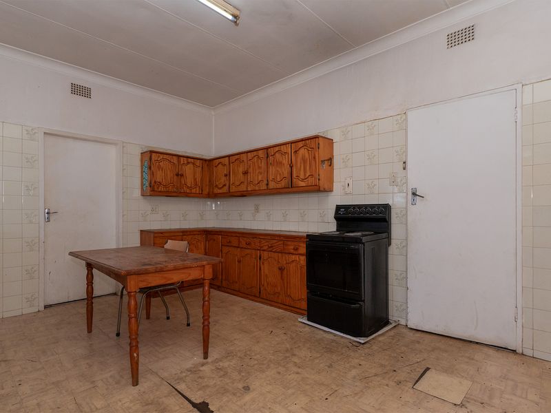 A dated kitchen featuring wooden cabinetry, tiled backsplash, and a freestanding stove, requiring modernization and flooring repairs.