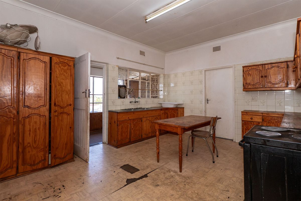A dated kitchen featuring wooden cabinetry, tiled backsplash, and a double sink, requiring significant renovation and flooring repairs to modernize the space.