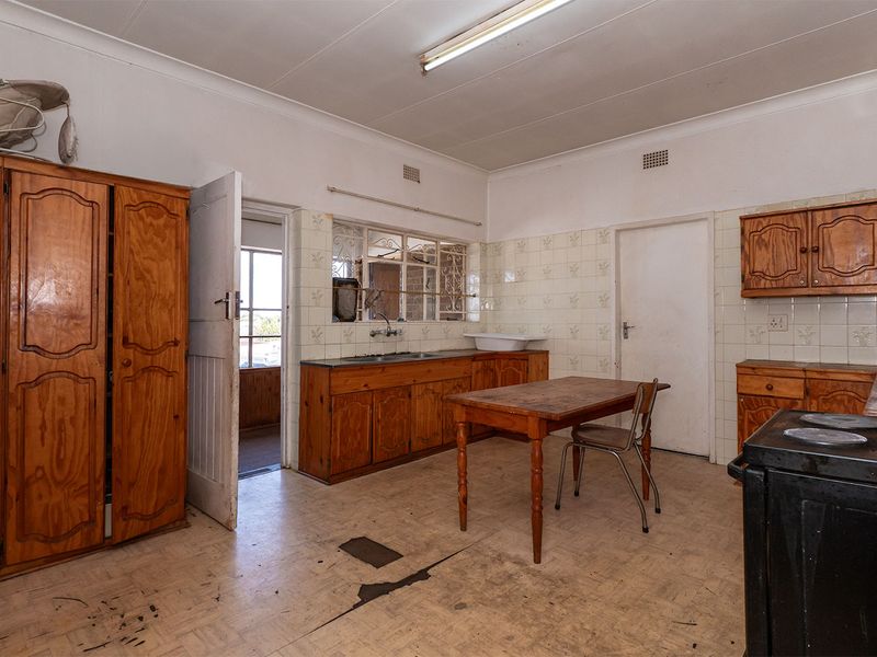 A dated kitchen featuring wooden cabinetry, tiled backsplash, and a double sink, requiring significant renovation and flooring repairs to modernize the space.