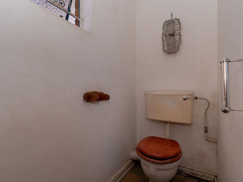 A small, dated bathroom featuring a standard toilet, grab rail, and security-barred window, requiring cosmetic updates to improve its overall condition.