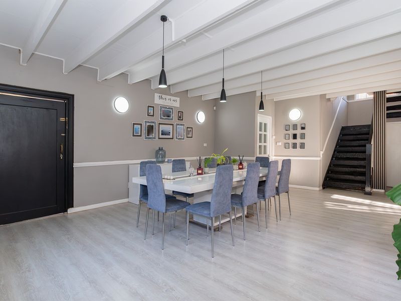A bright and modern dining room featuring exposed white ceiling beams, laminate flooring, and a staircase leading to the upper level.