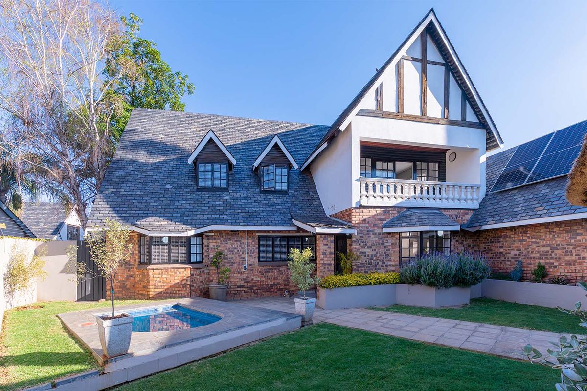 Rear view of a multi-story brick home featuring a slate roof, a balcony with balustrade, solar panels, and a small plunge pool set in a garden.