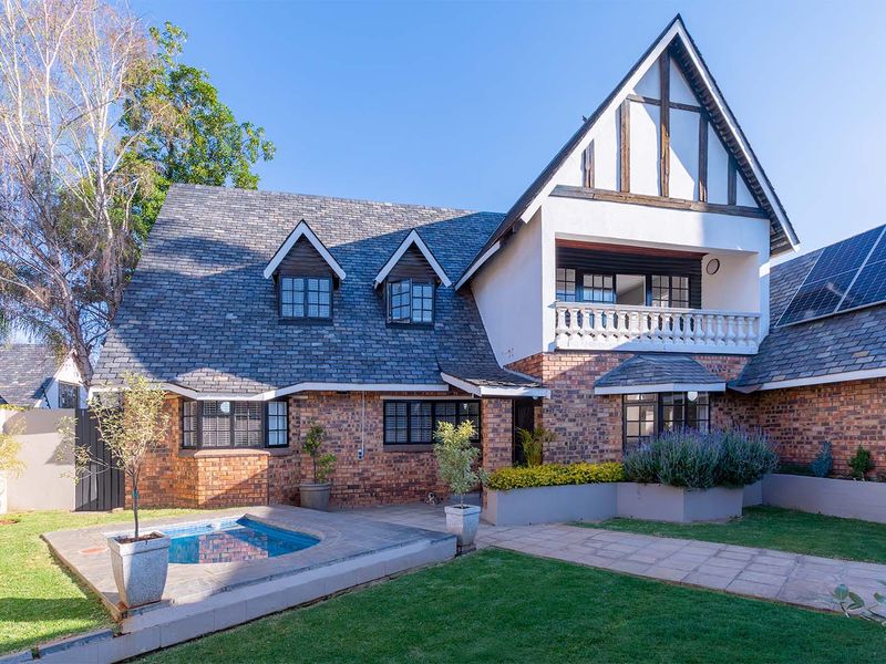 Rear view of a multi-story brick home featuring a slate roof, a balcony with balustrade, solar panels, and a small plunge pool set in a garden.