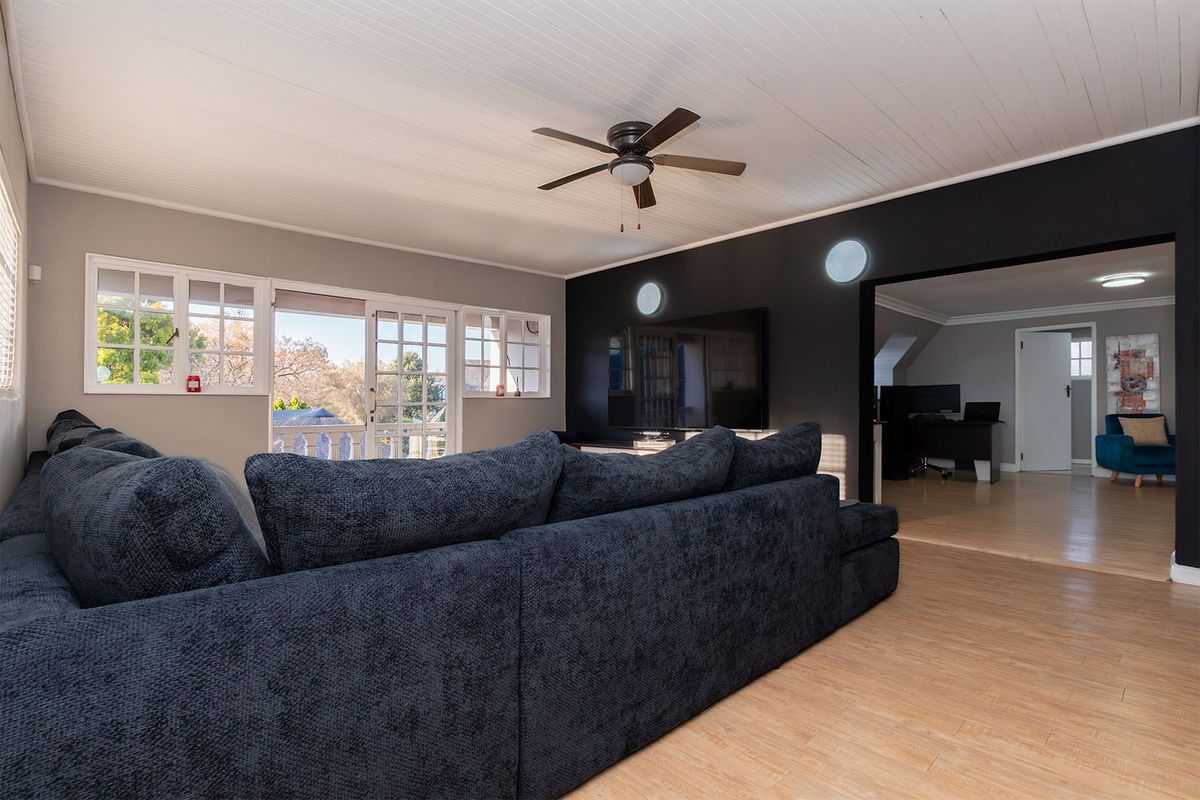 Spacious living room featuring laminate flooring, a ceiling fan, and sliding glass doors leading to an outdoor area, with an adjacent room visible.