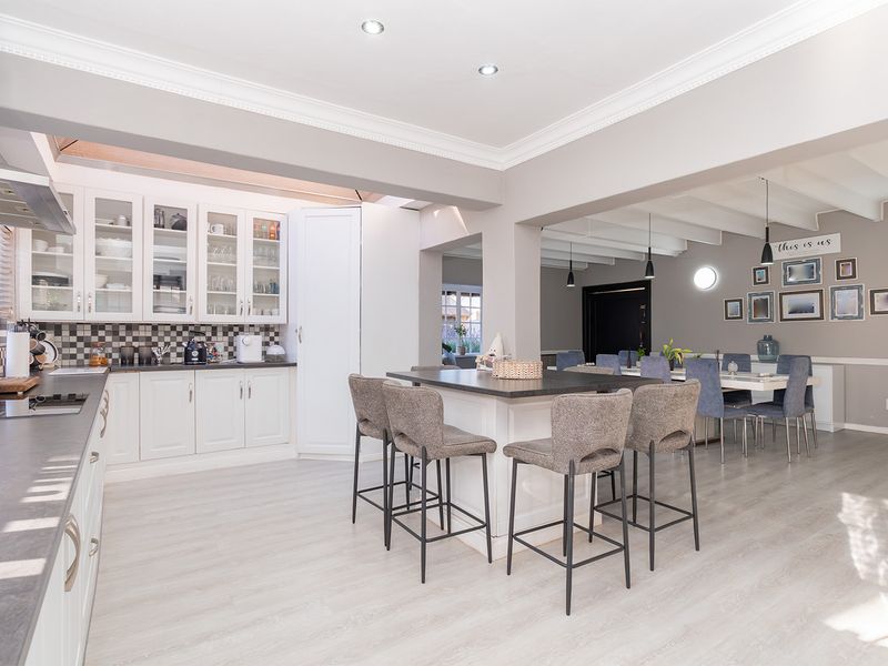 Spacious open-plan kitchen and dining area featuring white cabinetry, a central island, modern recessed lighting, and light-toned laminate flooring throughout.