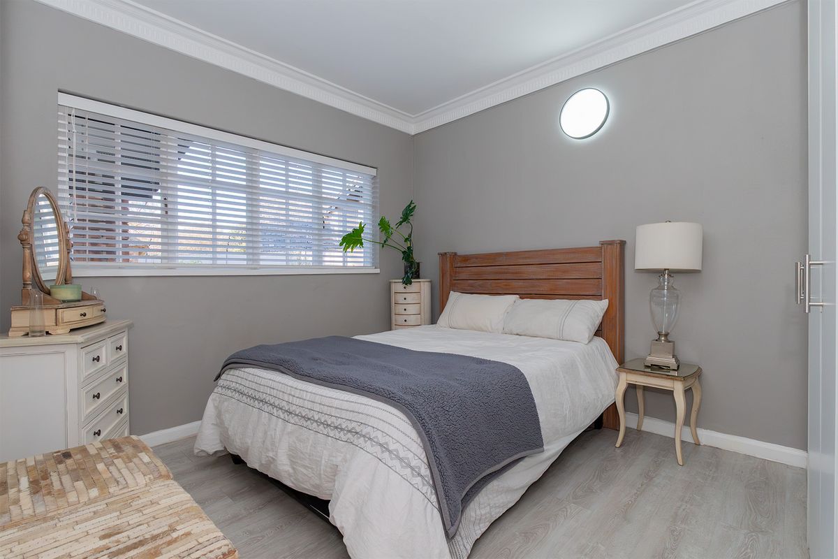 A well-maintained bedroom featuring neutral grey walls, crown molding, laminate flooring, and a large window with venetian blinds.