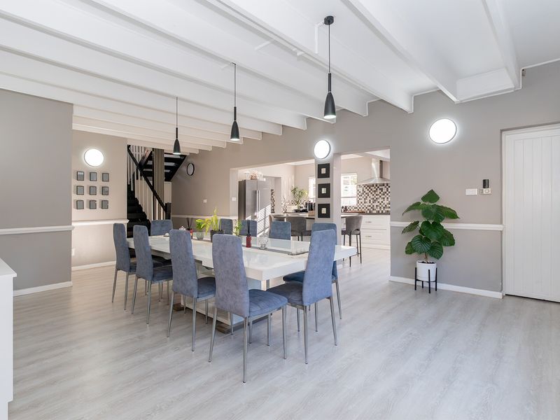 Spacious open-plan dining area featuring exposed beam ceilings, modern pendant lighting, and seamless flow into the adjacent kitchen space.