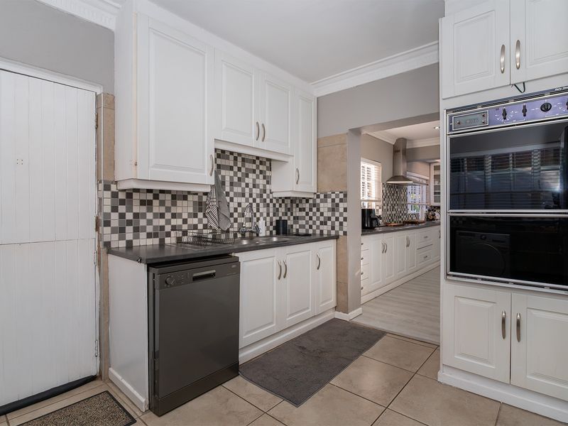 A functional scullery featuring white cabinetry, a double wall oven, tiled splashback, and direct access to the main kitchen area.