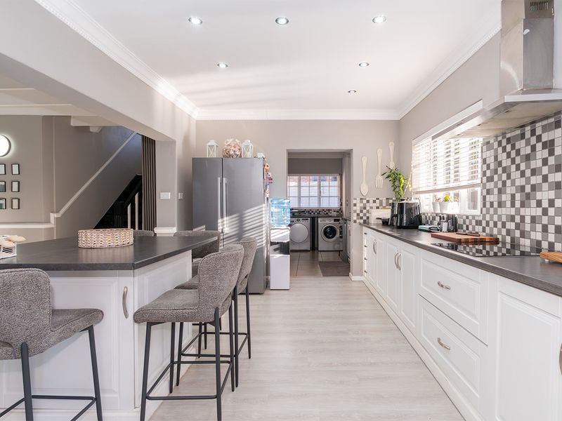Modern kitchen featuring a central island, white cabinetry, tiled backsplash, and integrated appliances, with an adjacent laundry area visible in the background.
