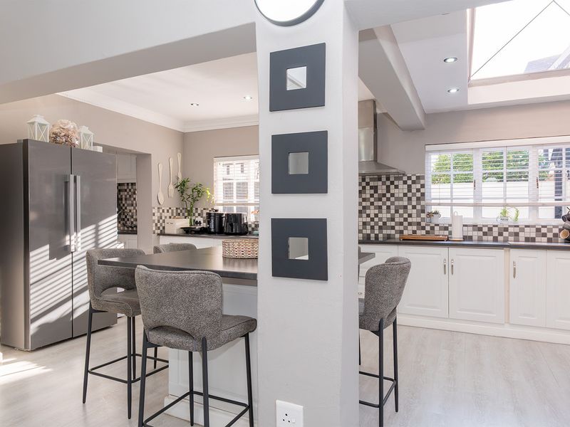 A bright open-plan kitchen featuring a central island, modern white cabinetry, a checkered tile backsplash, and a skylight providing ample natural light.