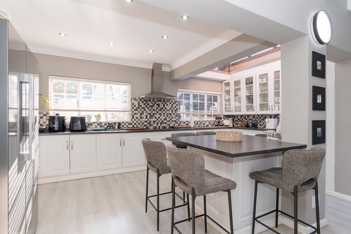 Modern kitchen featuring white cabinetry, a central island with seating, mosaic tile backsplash, and recessed lighting, creating a bright and functional culinary space.