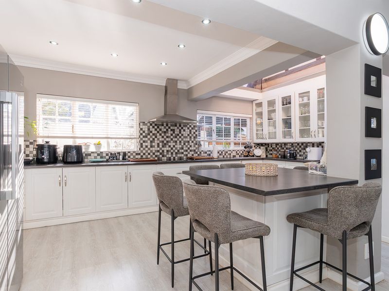Modern kitchen featuring white cabinetry, a central island with seating, mosaic tile backsplash, and recessed lighting, creating a bright and functional culinary space.