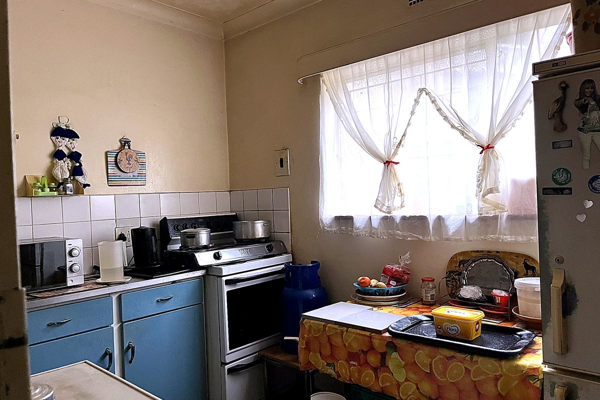 A compact, dated kitchen featuring original blue cabinetry, a tiled splashback, and a freestanding stove, offering potential for a modern renovation.