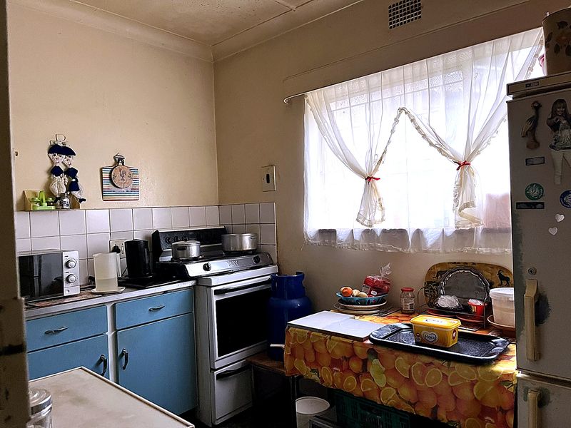 A compact, dated kitchen featuring original blue cabinetry, a tiled splashback, and a freestanding stove, offering potential for a modern renovation.