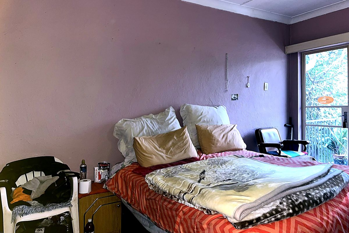 A bedroom featuring a sliding glass door leading to an outdoor area, with visible wall surface imperfections requiring maintenance.