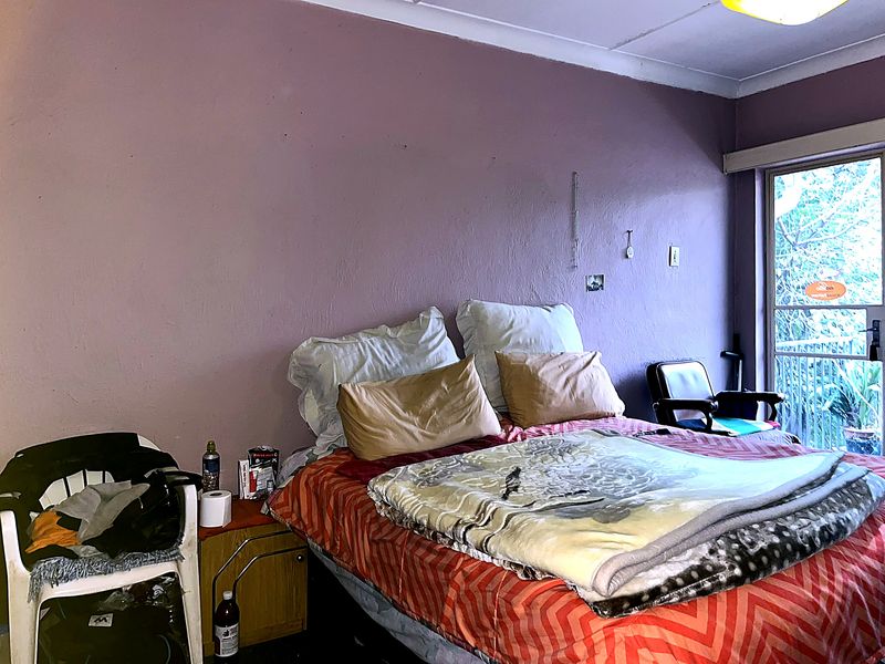 A bedroom featuring a sliding glass door leading to an outdoor area, with visible wall surface imperfections requiring maintenance.