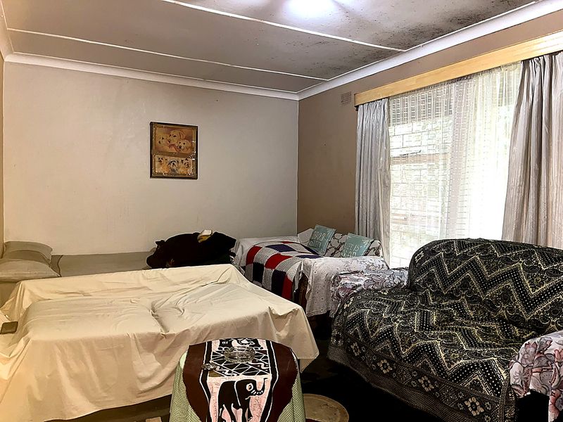 A bedroom featuring a large window and cove cornicing, currently showing significant ceiling staining and signs of wear requiring maintenance and cosmetic updates.