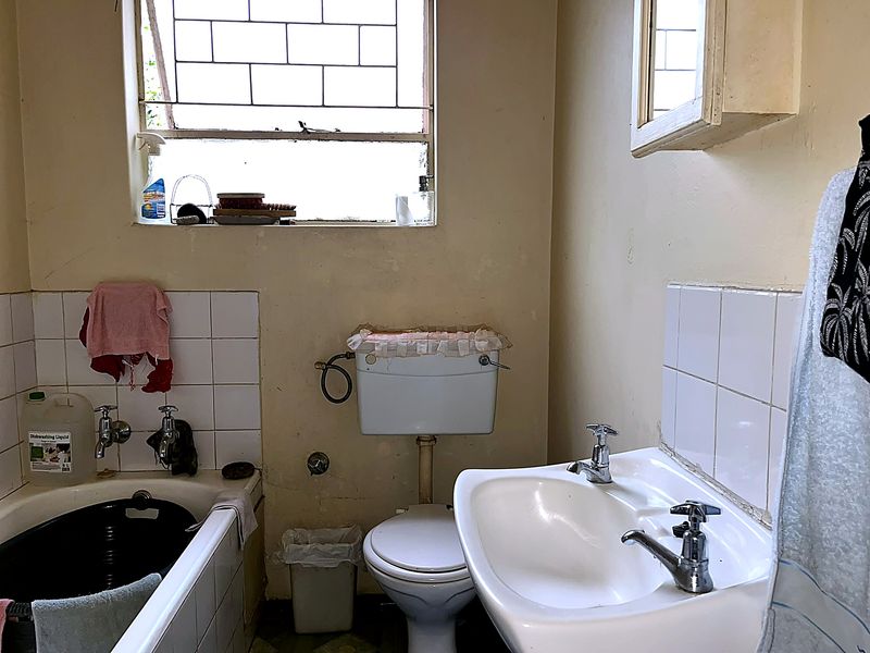 A dated bathroom featuring a bathtub, pedestal basin, and toilet, requiring cosmetic updates and refurbishment to improve its overall condition and aesthetic appeal.