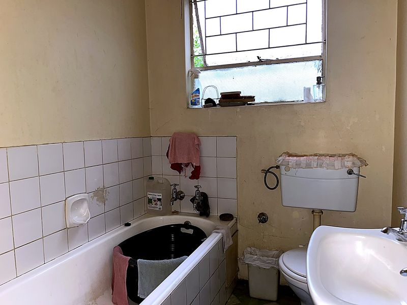 A dated bathroom featuring a bathtub, pedestal basin, and toilet, requiring significant cosmetic updates and repairs to wall finishes and fixtures.