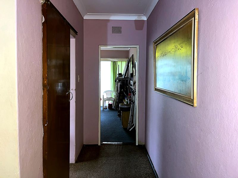 A narrow residential hallway featuring purple painted walls, carpeted flooring, and a timber door leading to an adjacent room.