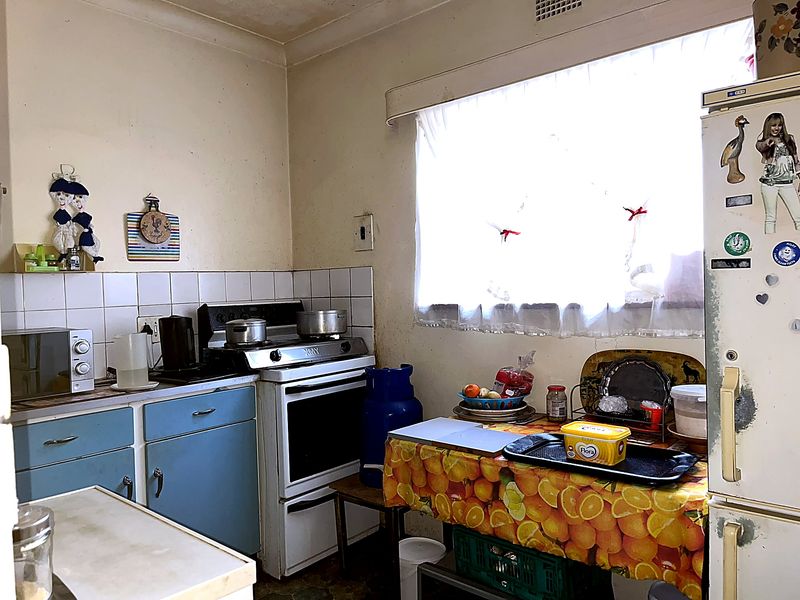 A dated kitchen featuring original cabinetry, a tiled splashback, and a freestanding stove, requiring cosmetic updates and modernization to improve functionality and aesthetic appeal.