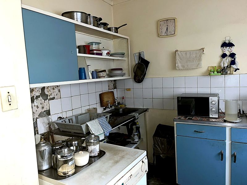 A dated kitchen featuring blue cabinetry, a tiled backsplash, and a stainless steel sink, currently showing significant signs of wear and surface damage.