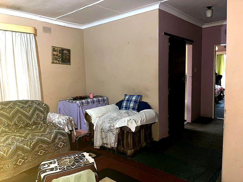 A dated living room area featuring a sliding door, ceiling cornices, and visible wear on the ceiling and flooring finishes.