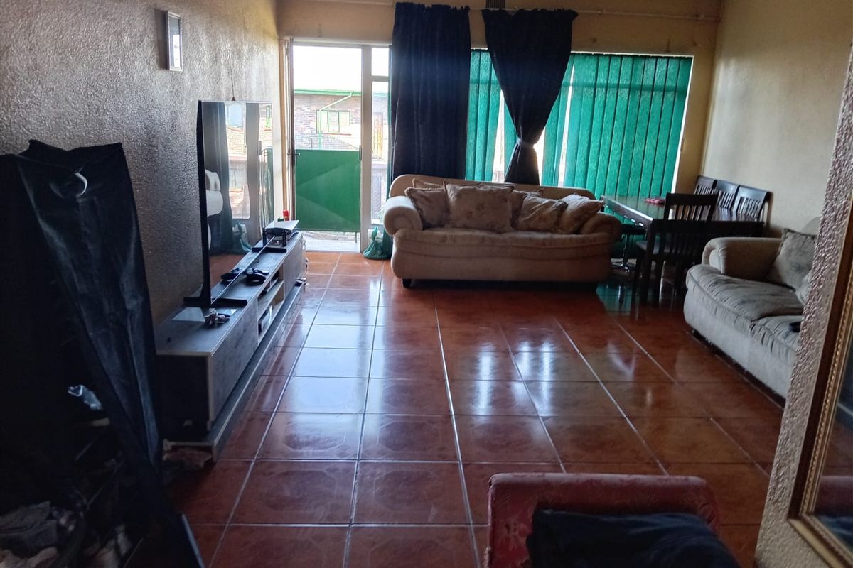 A living room featuring tiled flooring, a sliding glass door leading to an outdoor area, and vertical blinds.