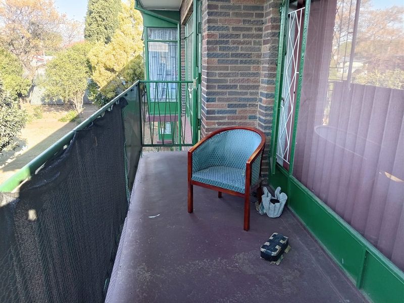 A balcony area featuring a brick facade, metal balustrade, and sliding glass door access, overlooking the surrounding garden area.