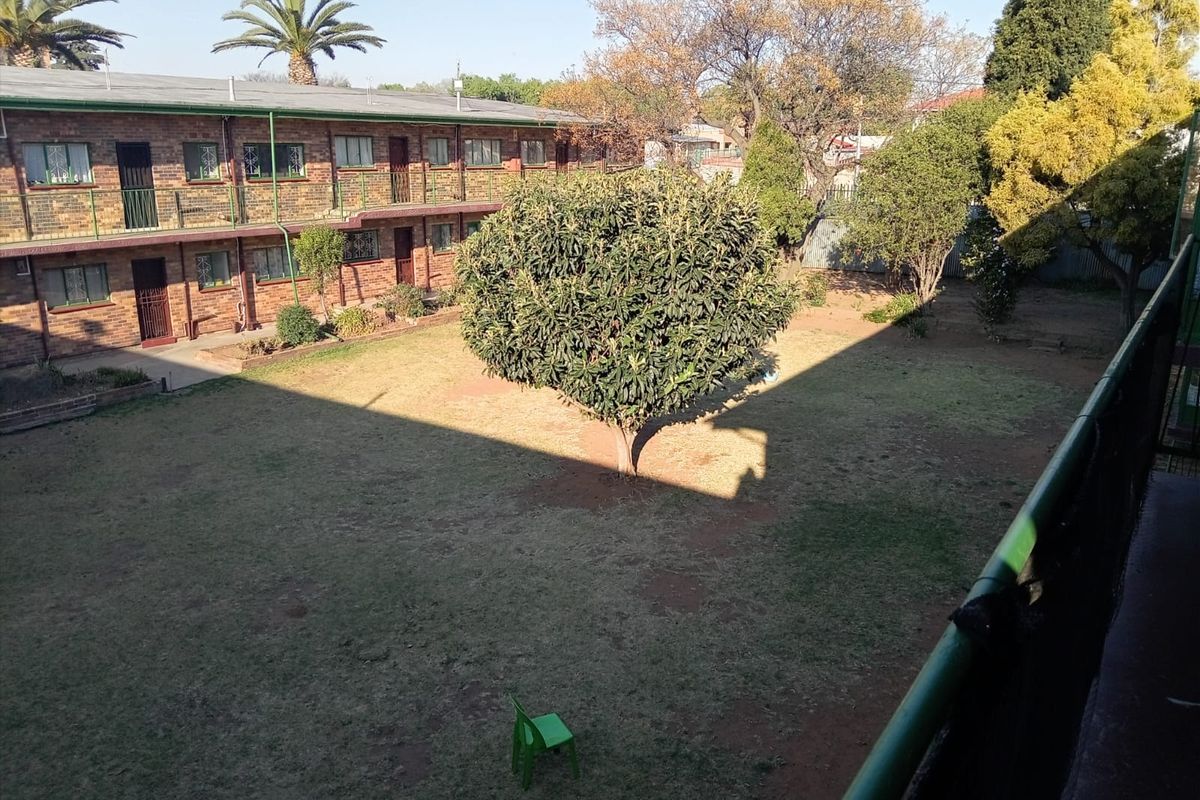 View of the communal garden and rear brick facade of the apartment complex from an elevated balcony.