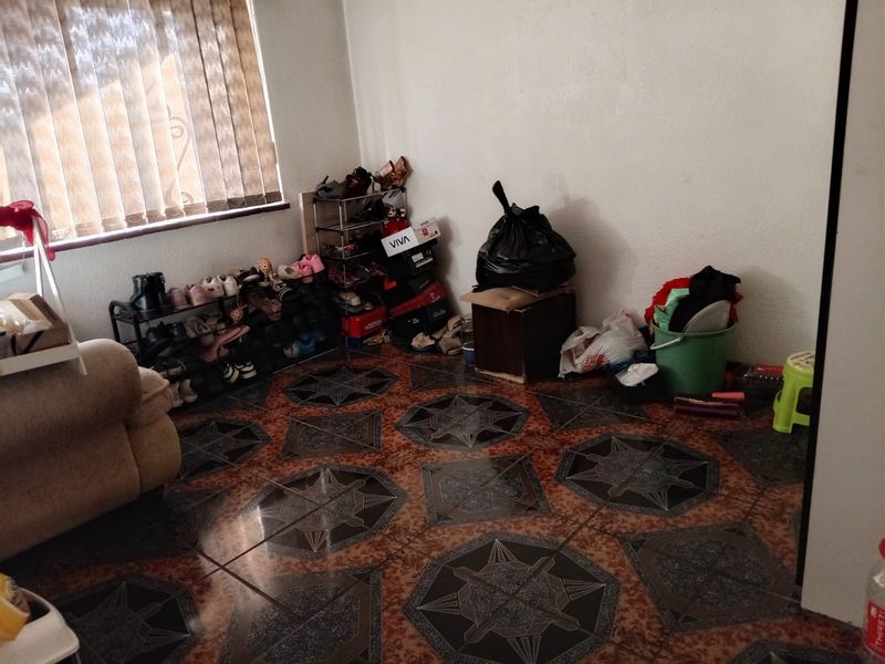 A living room area featuring patterned floor tiles and vertical window blinds, currently used for storage.