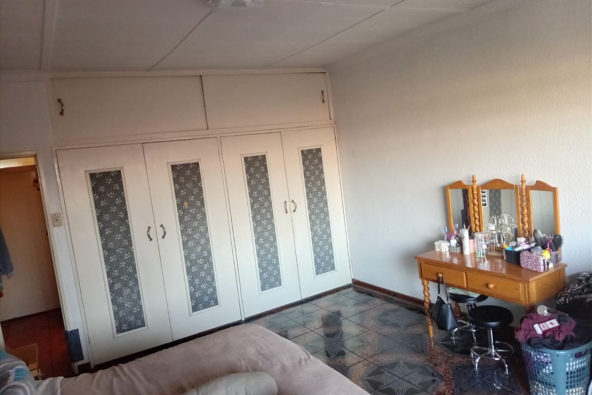 A bedroom featuring built-in cupboards with decorative panels and tiled flooring, offering a functional space with potential for cosmetic updates.