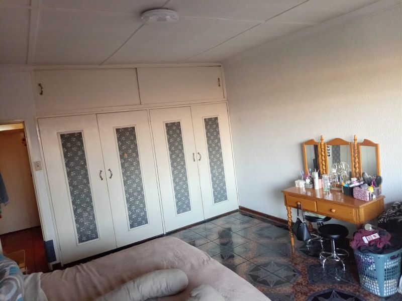 A bedroom featuring built-in cupboards with decorative panels and tiled flooring, offering a functional space with potential for cosmetic updates.