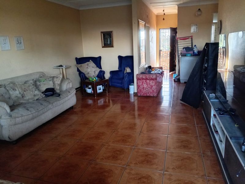Spacious living area featuring ceramic floor tiles and a security gate entrance, offering a functional layout with neutral wall finishes.