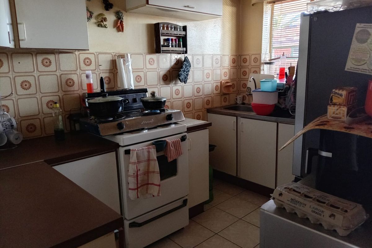 A functional kitchen featuring dated cabinetry, laminate countertops, a ceramic tile backsplash, and a freestanding stove with a window providing natural light.