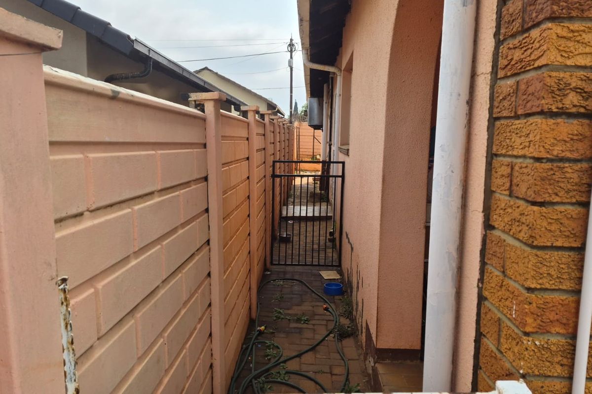 A narrow side passage featuring a precast concrete boundary wall, paved flooring, and a metal security gate leading to the rear of the property.