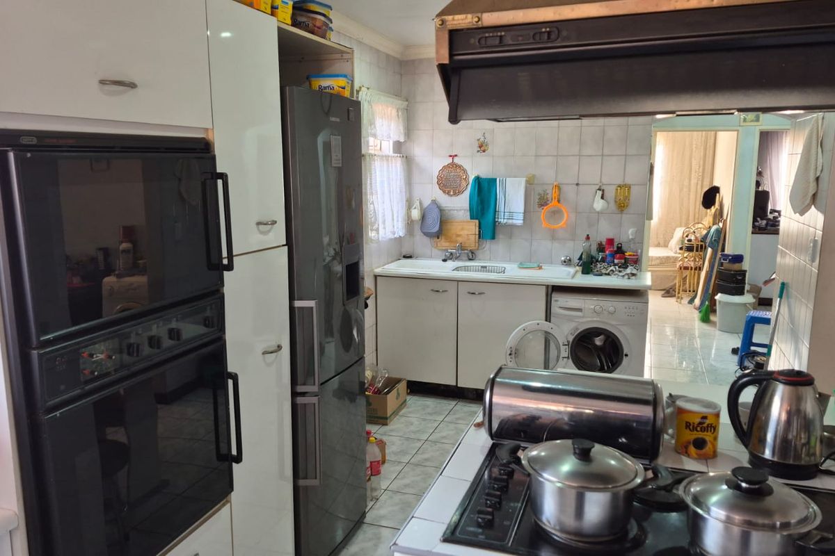 A functional kitchen featuring built-in ovens, a gas hob, extractor fan, and tiled finishes, offering potential for modernization and layout optimization.