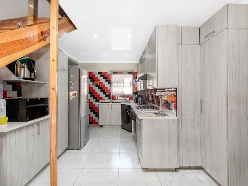 Modern kitchen featuring light wood-grain cabinetry, a striking red and black tiled backsplash, gas hob, extractor fan, and sleek white floor tiles.